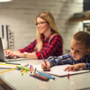 Female working on laptop with little boy coloring on paper next to her