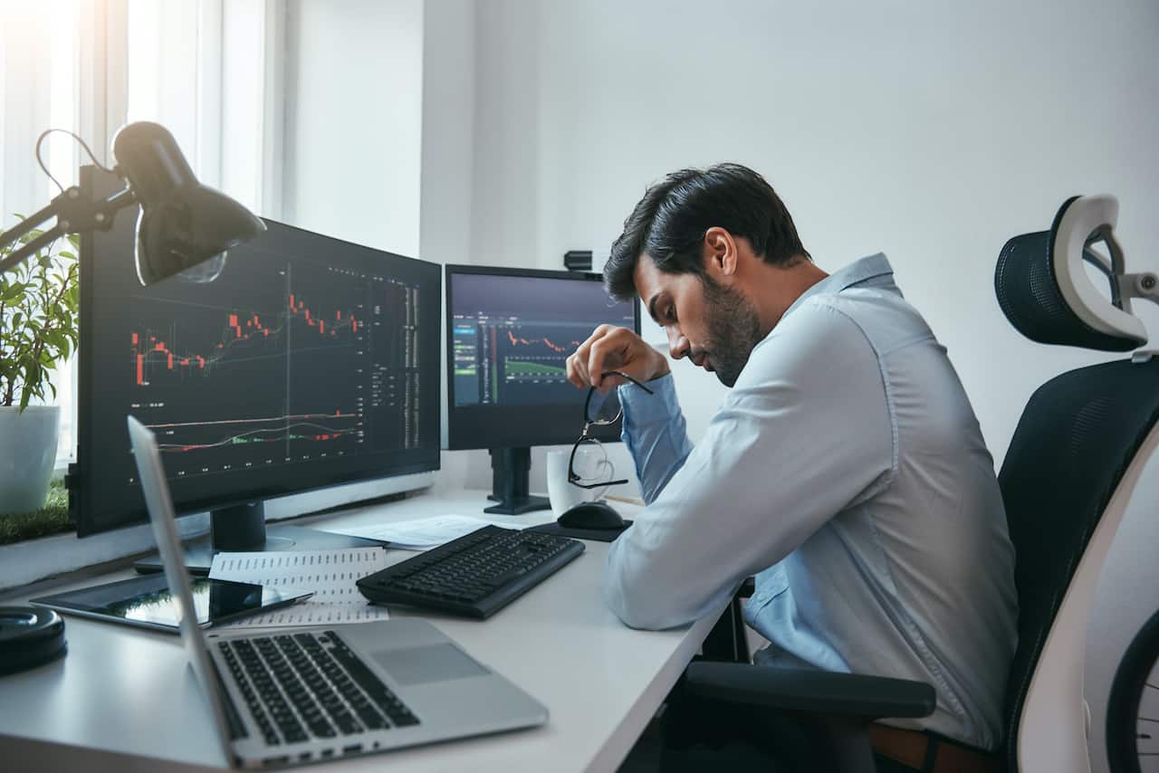 Tired IT technician working on two monitors and laptop